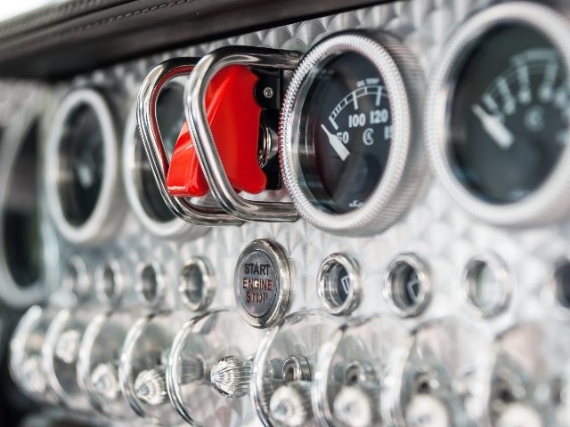 Dashboard of a Spyker sports car with round needle gauges embedded in patterned brushed chrome